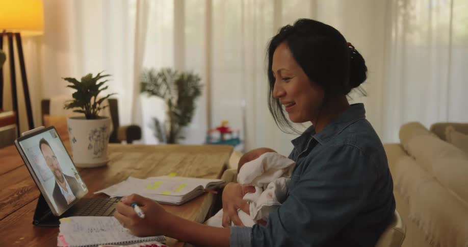 A mother holds her baby while talking on the tablet
