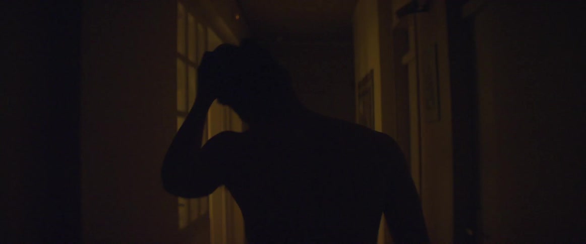 Shirtless man walking down the hallway of a house and then entering a room to the left