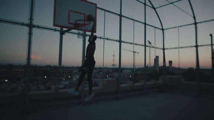 A man wearing headphones playing basketball alone