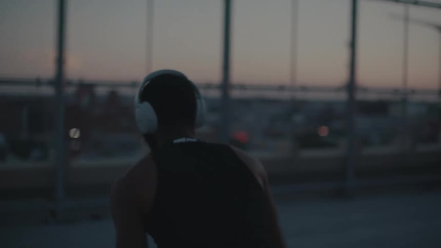 A man wearing white headphones practices basketball at sunset