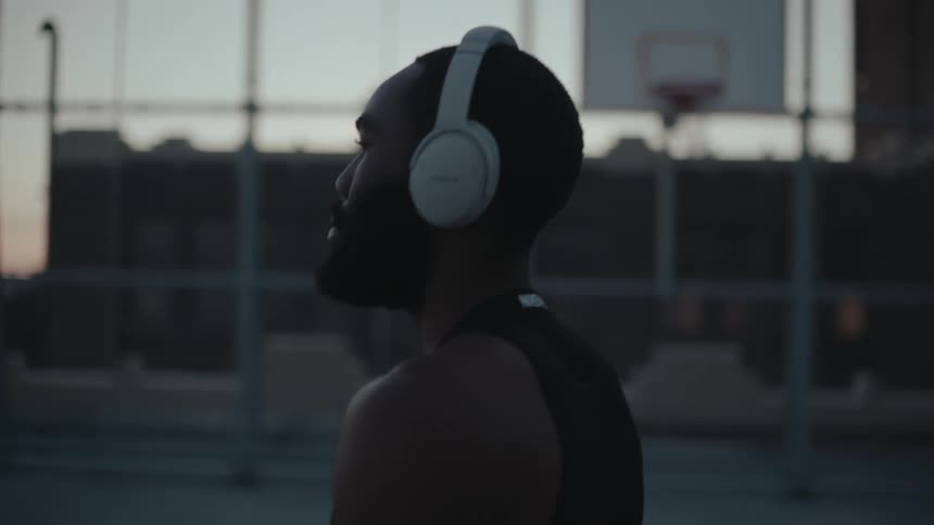 Man wearing headphones carries basketball across outdoor basketball court after dusk