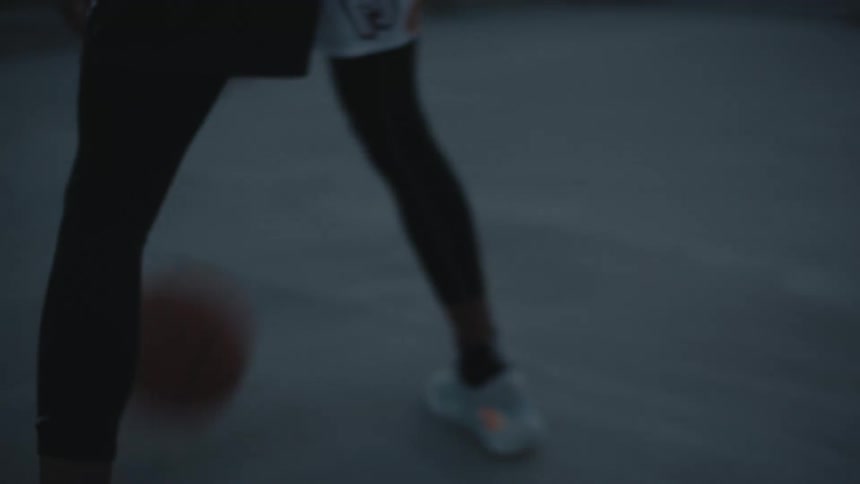 Male basketball player dribbles on basketball court overlooking city at sunset