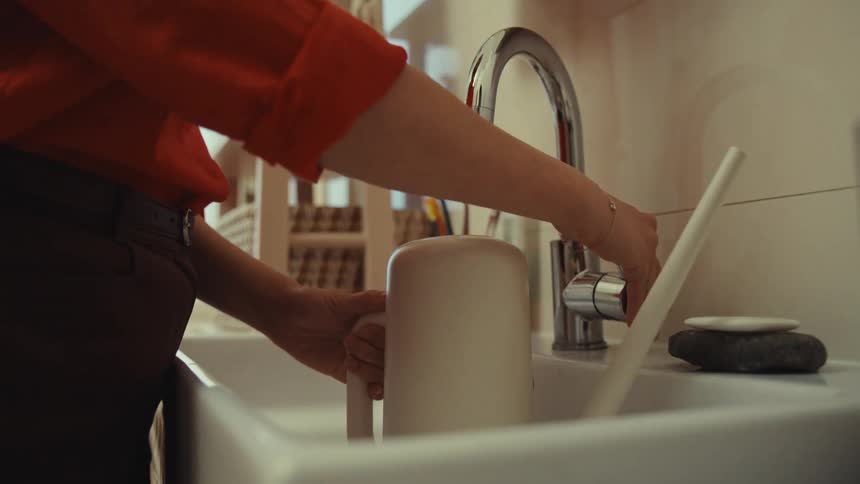 A woman fills a watering can in the sink
