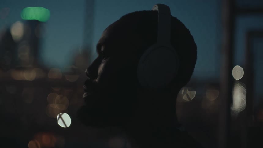 Side portrait of a man with headphones and observing a metropolis at night