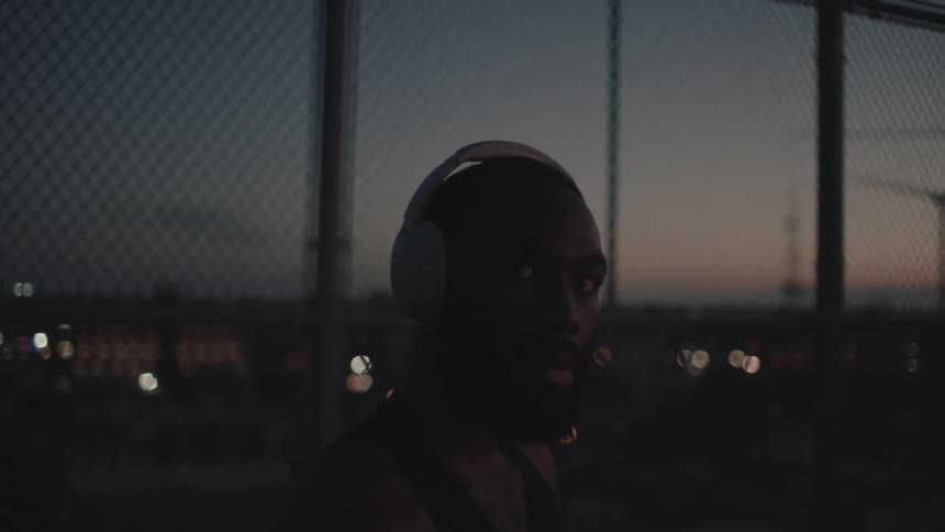 A man is wearing a white headset in a place with a fence behind at dusk