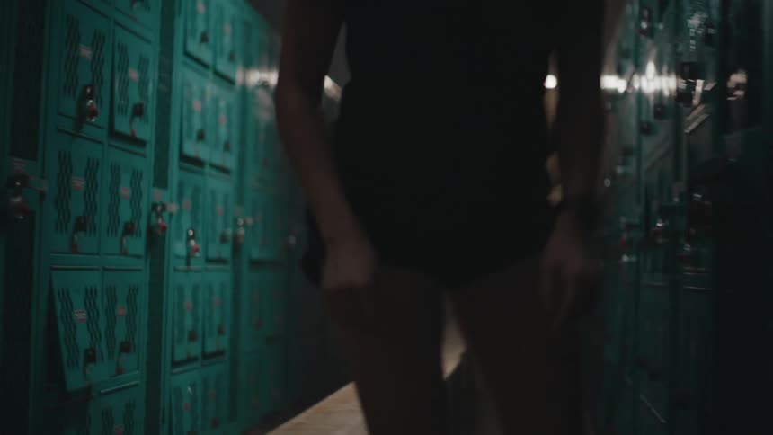 F a woman wearing earphones a ponytail a black tshirt and shorts standing up off a bench in the locker room