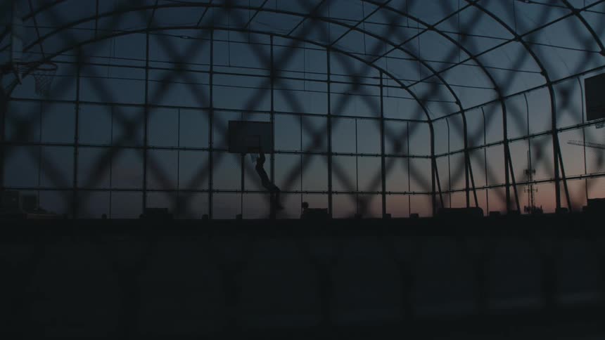 A man dunks the basketball at dusk