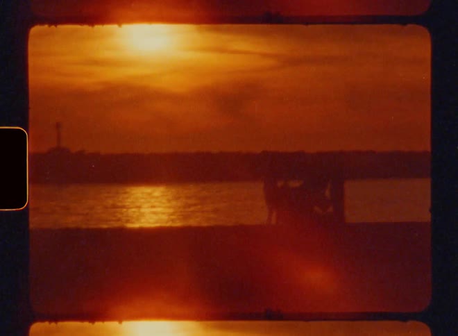 Sunset over a body of water with silhouettes of people near the shore caught on vintage film