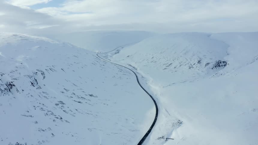 Aerial scenery of a winding and narrow road in the middle of snowy mountains