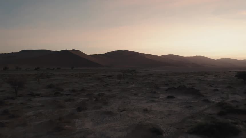 Landscape of a desert biome soil as the silhouette of mountains on the horizon in a reddish sky
