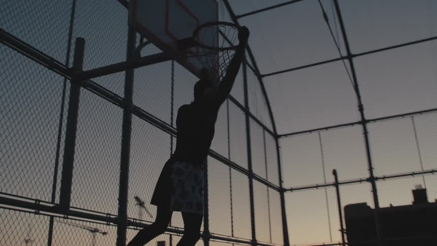 A black man slam dunks a basketball