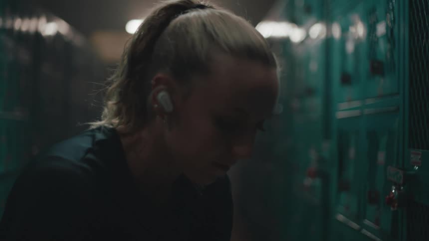 A woman listens to earbuds in a locker room