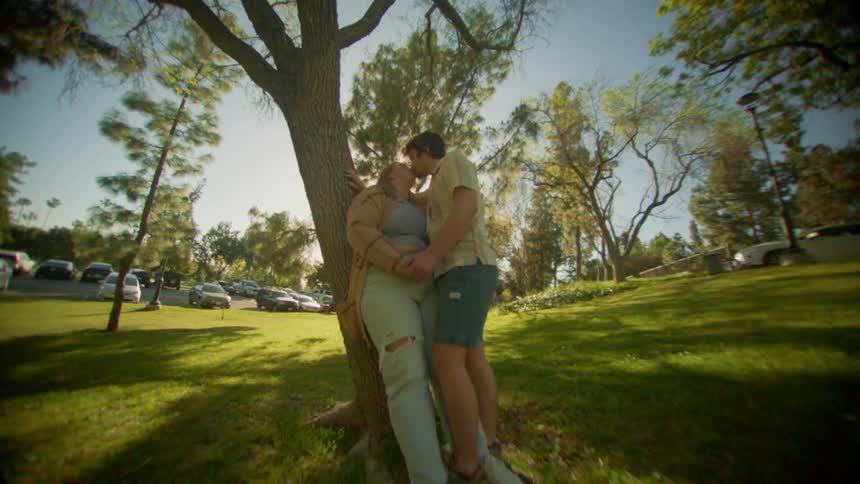Couple leans against tree in park while kissing