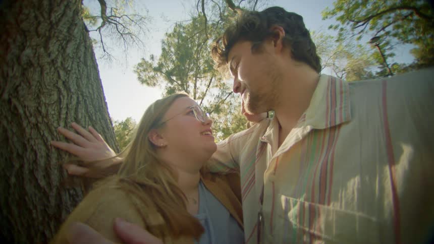 A man and a woman leaning against a tree caressing and smiling at each other
