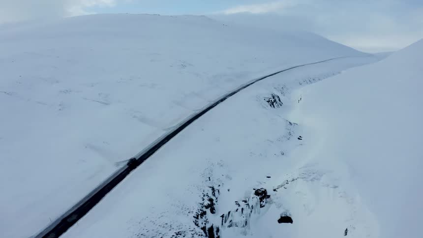 Aerial panorama of a black vehicle traveling on a narrow road in the middle of snowcovered mountains