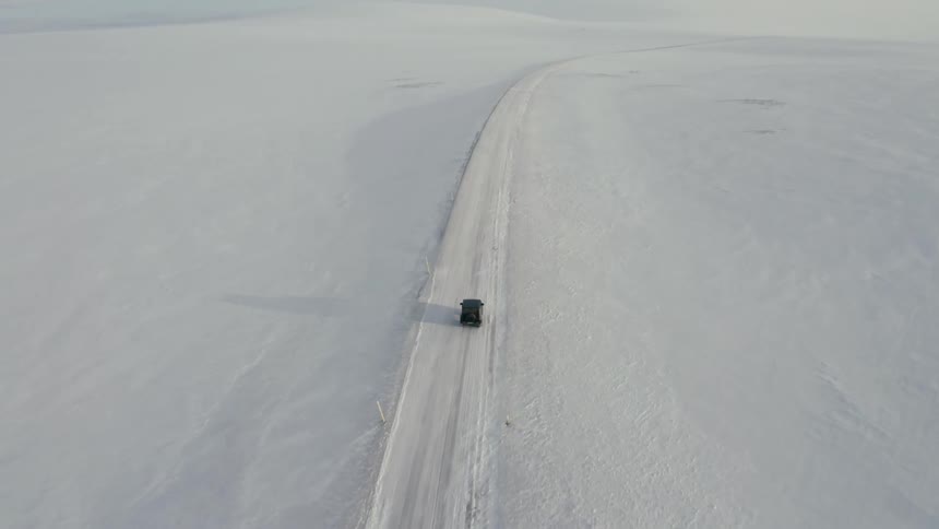 Vehicle drives along snow covered road through a snowy plain