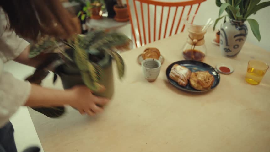 A woman removes a potted plant from a breakfast table