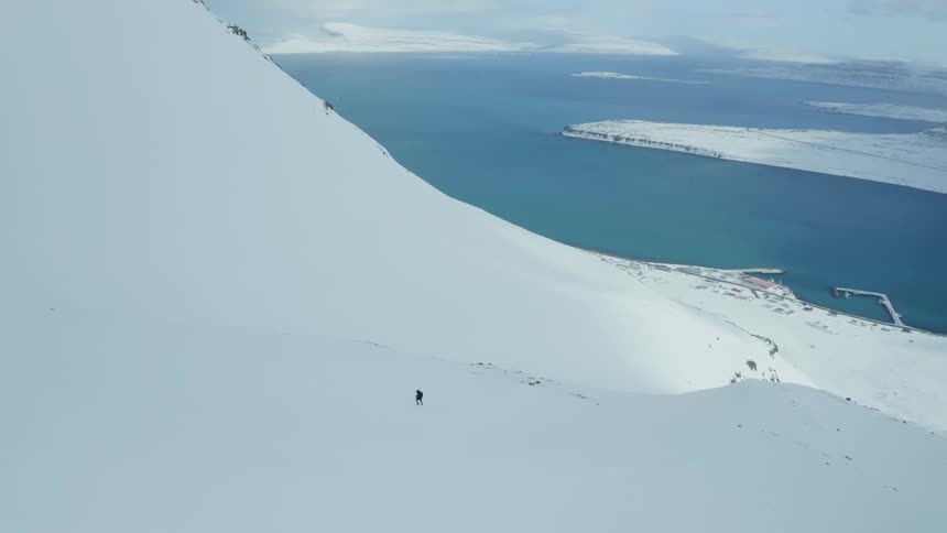 A person walks up a snow covered mountain near a coast