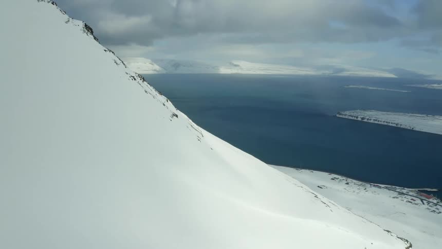 The side of an arctic mountain range the ocean visible in the distance
