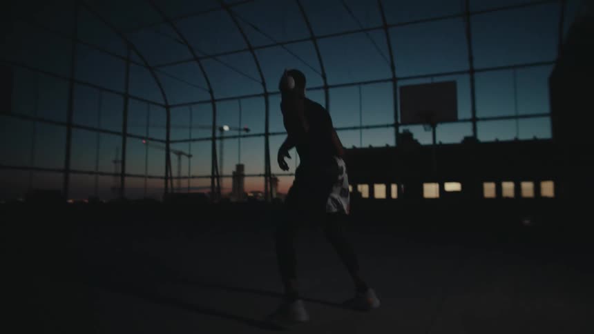 Man with headphones playing basketball on a terrace at night