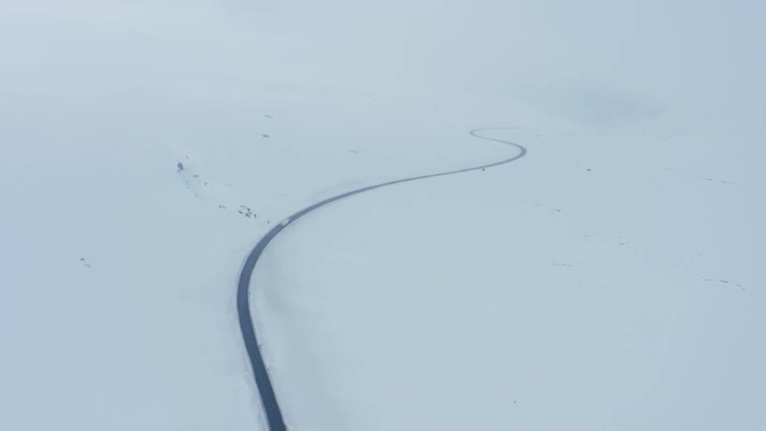 Aerial panorama of a long winding road surrounded by snowy mountains on a foggy day