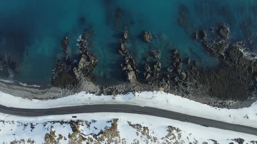 Aerial of a highway along a snowy mountainous coastline