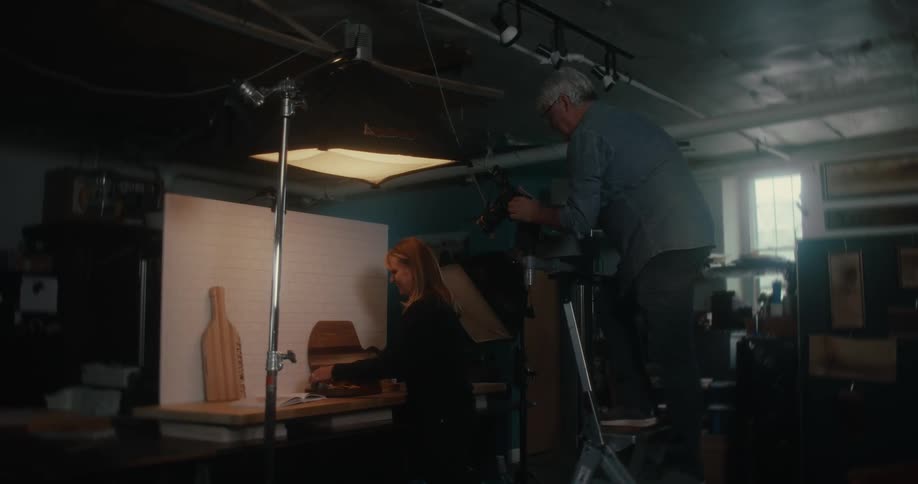 Man on top of a ladder photographing a woman organizing utensils on top of rustic wood