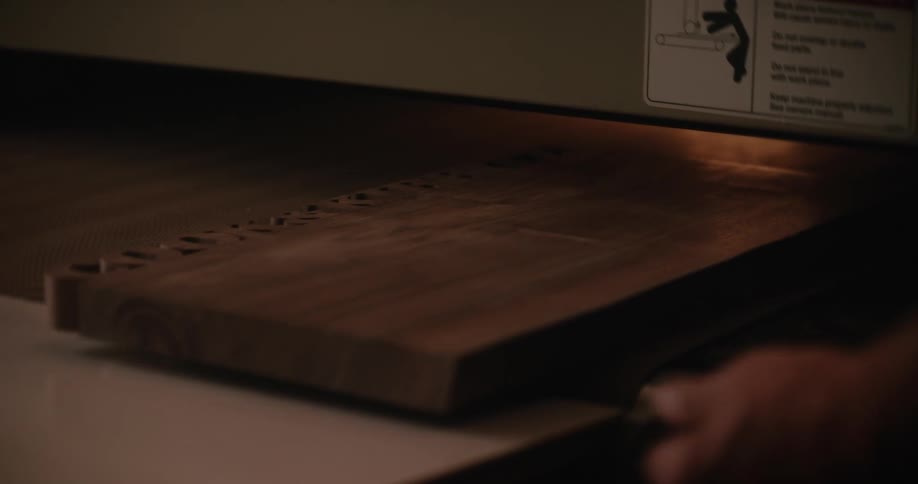 A man removes a piece of cured wood from an oven conveyor belt