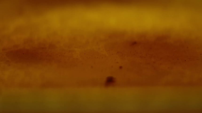 A liquid with hues of yellow and orange ripples as it flows