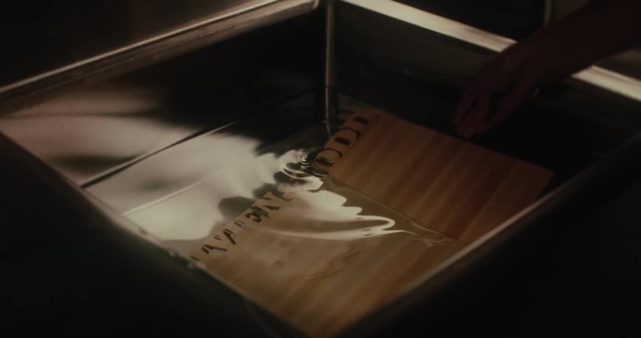 A wooden board is placed in a sink filled with water by a human hand