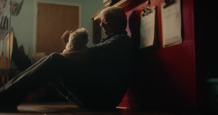Older man sits on floor petting a small dog