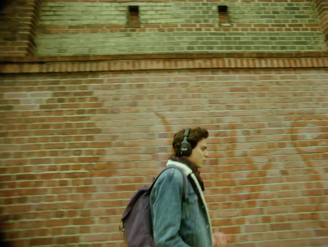 Man listening to headphones walks past graffiti covered building wall