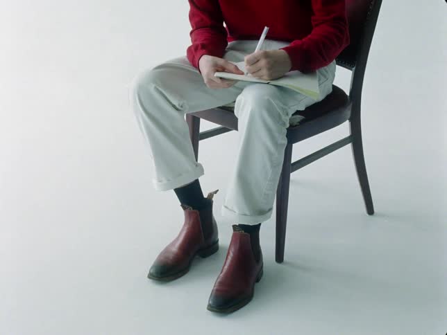 A man sits in a chair while writing in a notebook