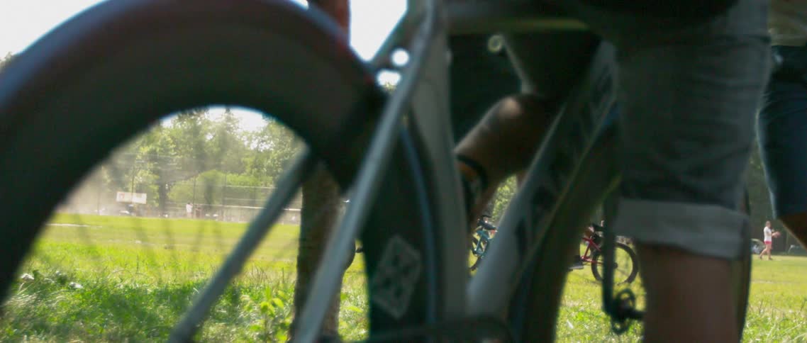 A group of four cyclists is riding in slow motion through a busy park at midday