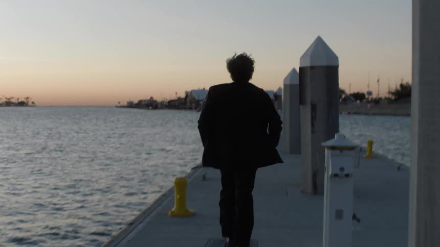 Man in suit seen from behind running on a seaside dock in an orange sky on the horizon