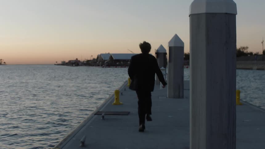 Man in suit seen from behind running on seaside dock in a morning sky
