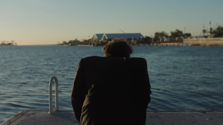 View of a man crouching and wearing black business clothes on a seaside dock in the morning