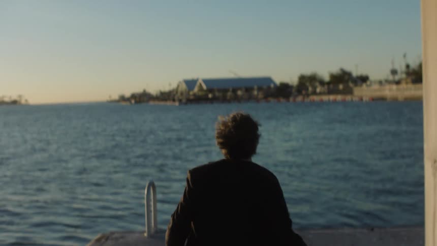 A sad man in a suit runs up to the end of a pier and gets down on his knees