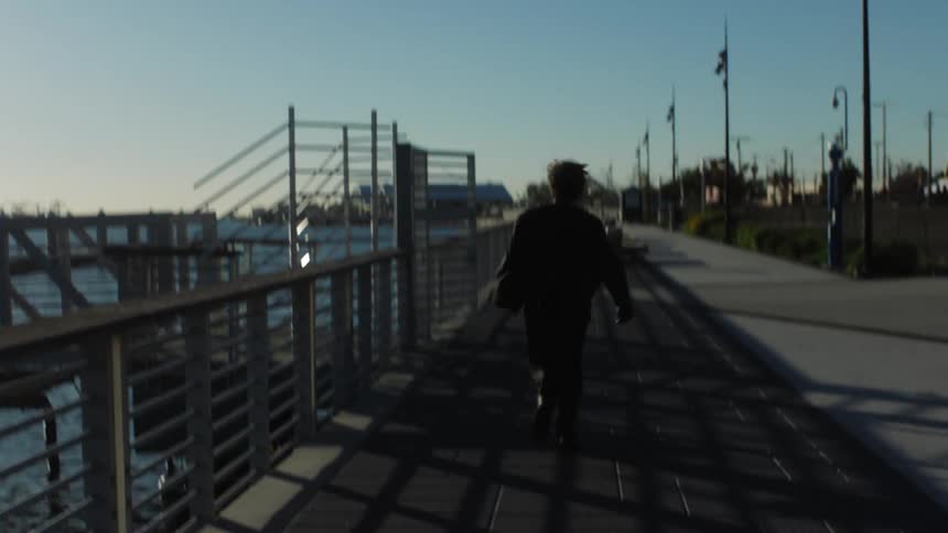 A person has their back turned and is running on a deck next to the water