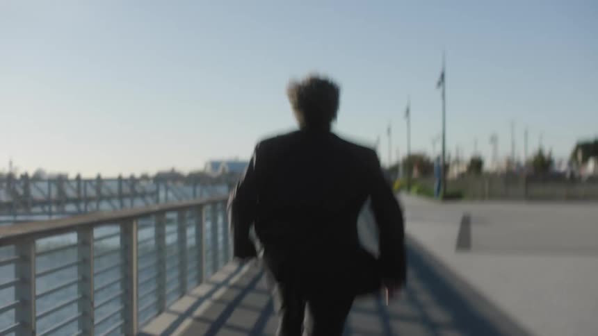 Man wearing suit runs along path paralleling waterfront