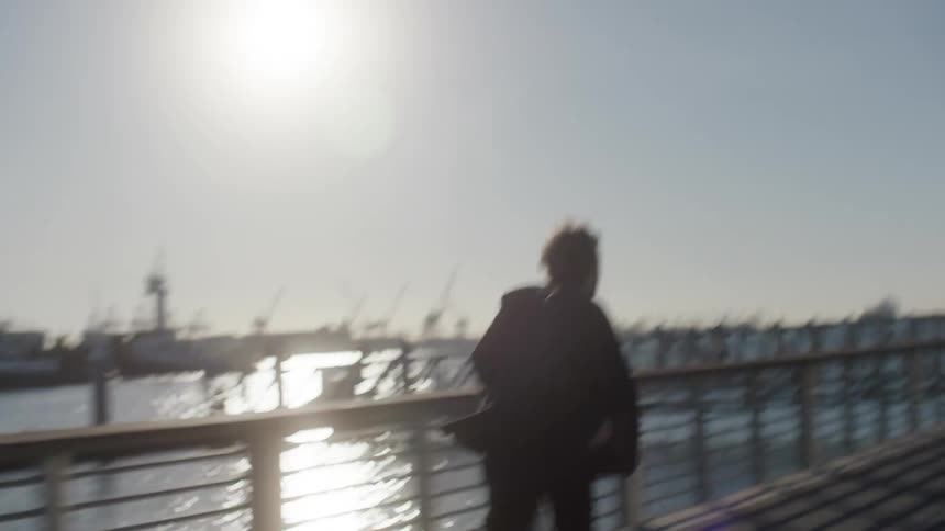 A man anxiously running down the promenade is silhouetted against the sun