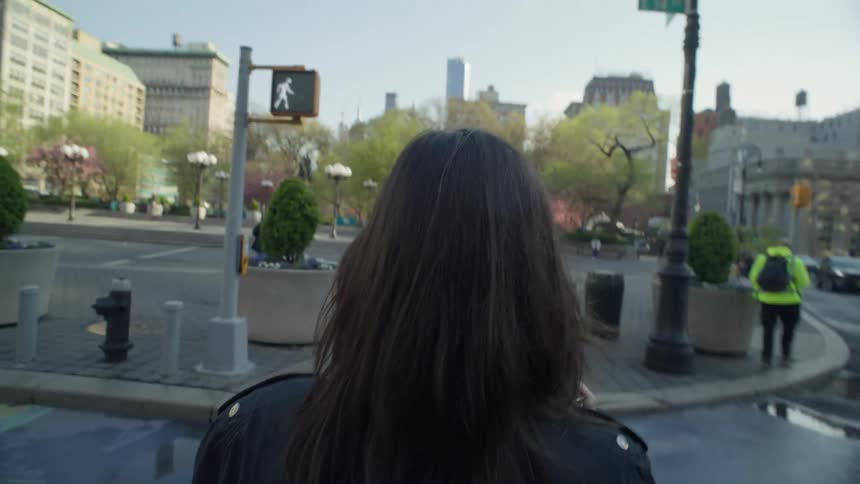 Perspective of a woman seen from behind crossing the street of a metropolis with buildings around it and vehicle traffic