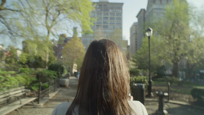 A woman drinks coffee while walking through the park