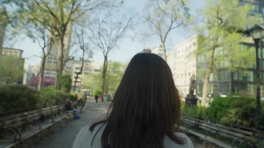 A woman walks through a park and sits on a bench sipping coffee