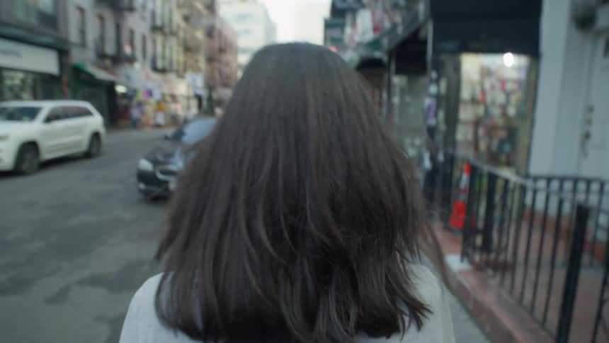 Female pedestrian walks along city sidewalk passing a restaurant with outdoor seating