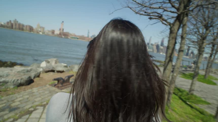 A woman walks in the park then sits on a bench to watch the city skyline