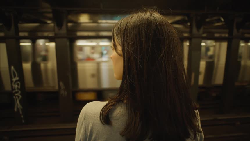 A young woman walks up to a subway platform and waits for the train