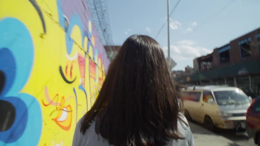 Woman walking down a sidewalk next to walls full of graffiti in NYC