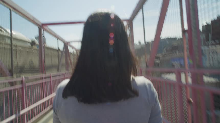 A woman is walking across an elevated pedestrian pathway in a city
