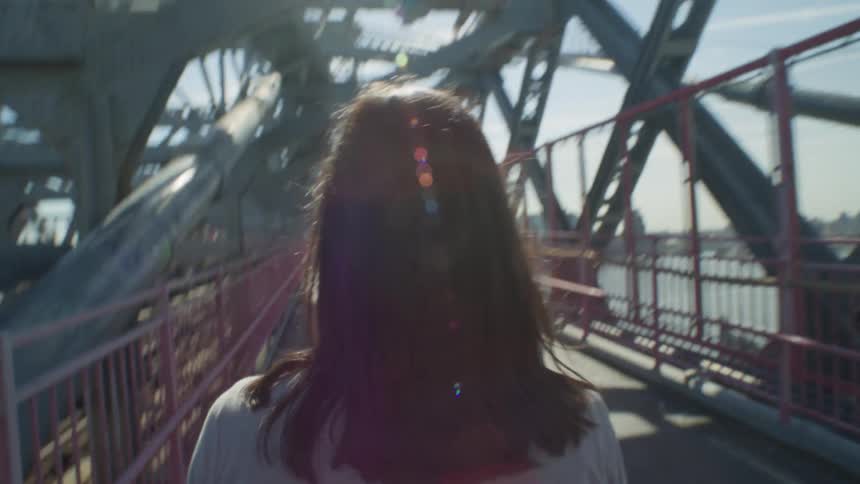A young woman walks across a bridge in a metropolitan area